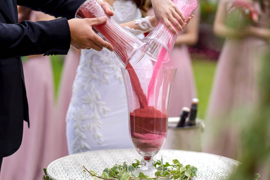 Hochzeitspaar schüttet bunten Sand in eine Vase